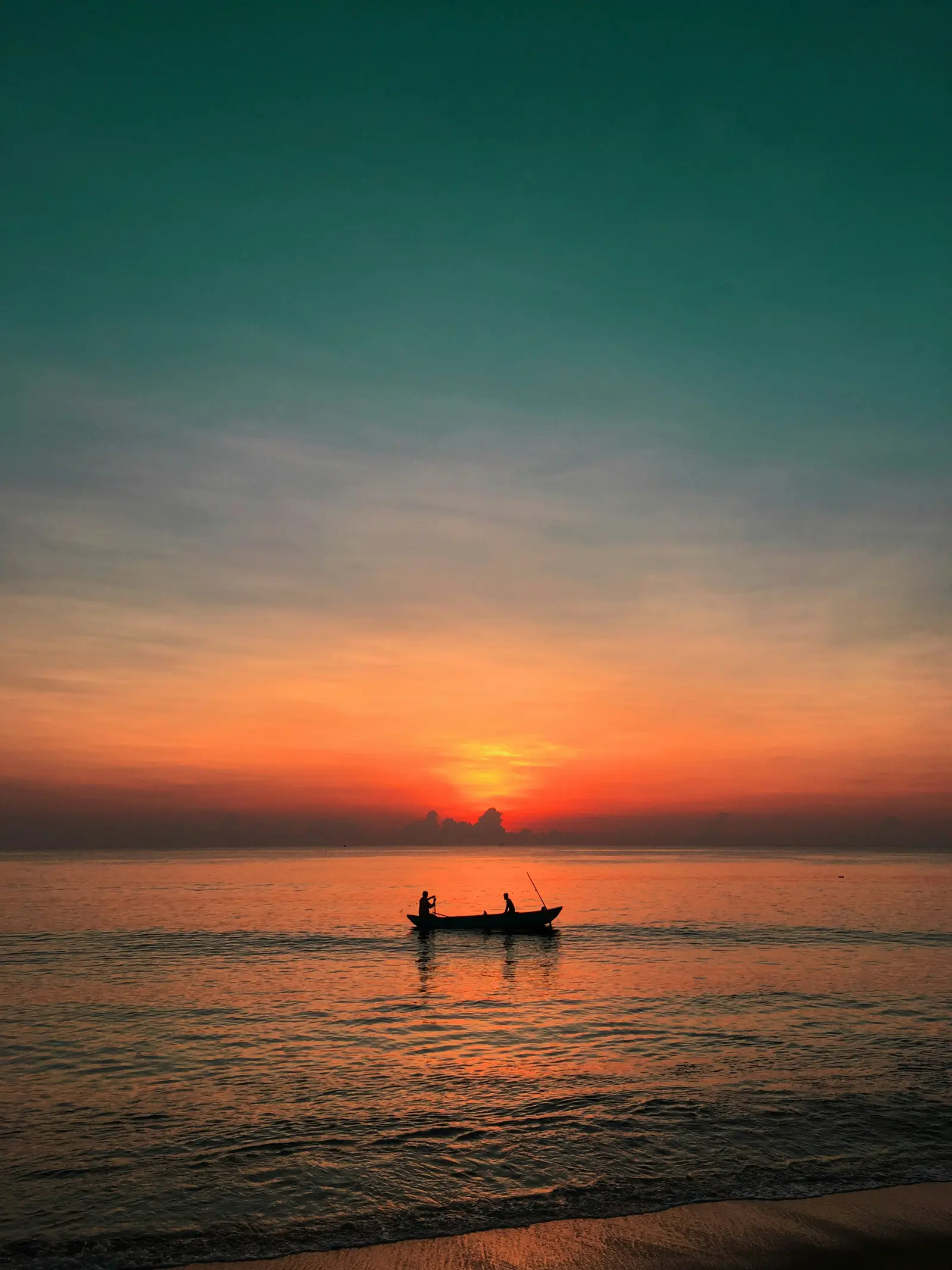 Fishermen in outrigger canoe silhouette on calm ocean at sunset
